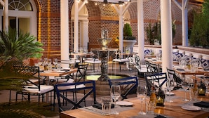 An outdoor dining area with brick walls, white columns, and string lights. Tables are set with wine glasses and plates. - The Hotel At Auburn University (Auburn)