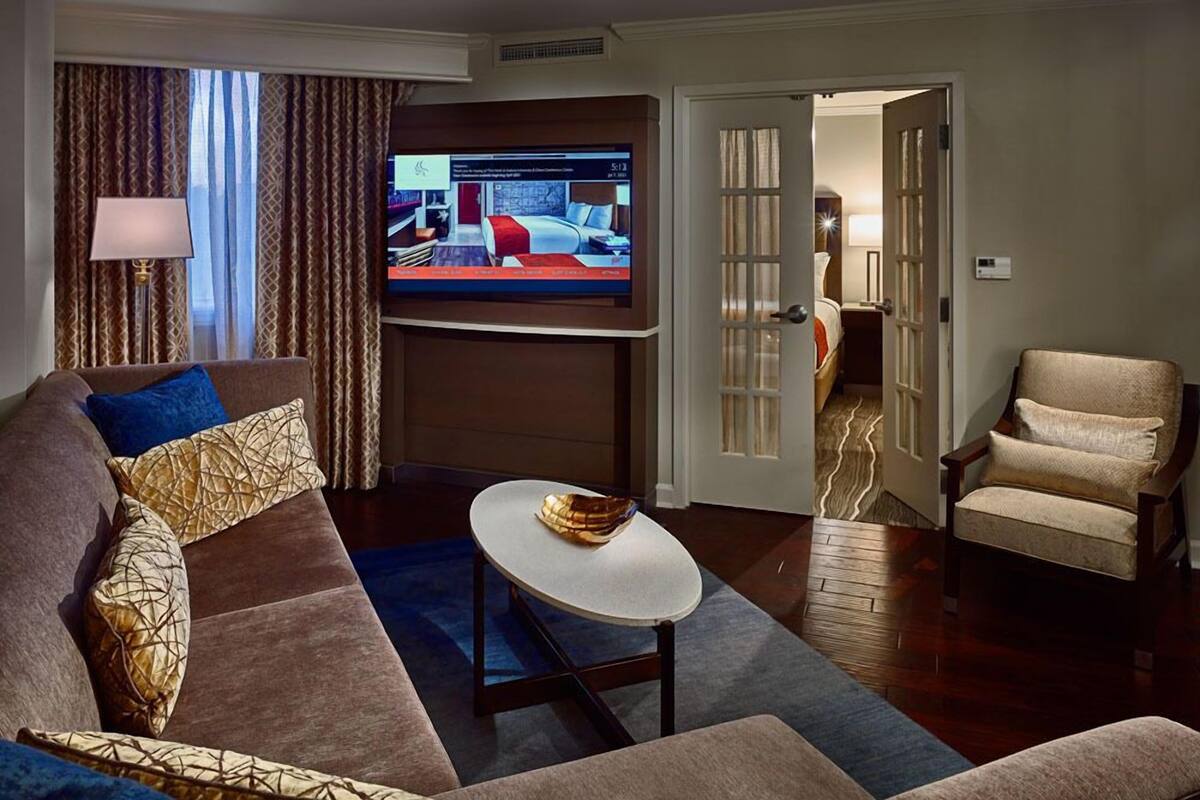 A modern living room with a large flat-screen TV, a sofa with patterned cushions, a round coffee table, and a chair.