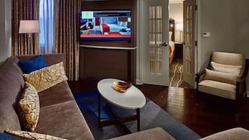 A modern living room with a large flat-screen TV, a sofa with patterned cushions, a round coffee table, and a chair.