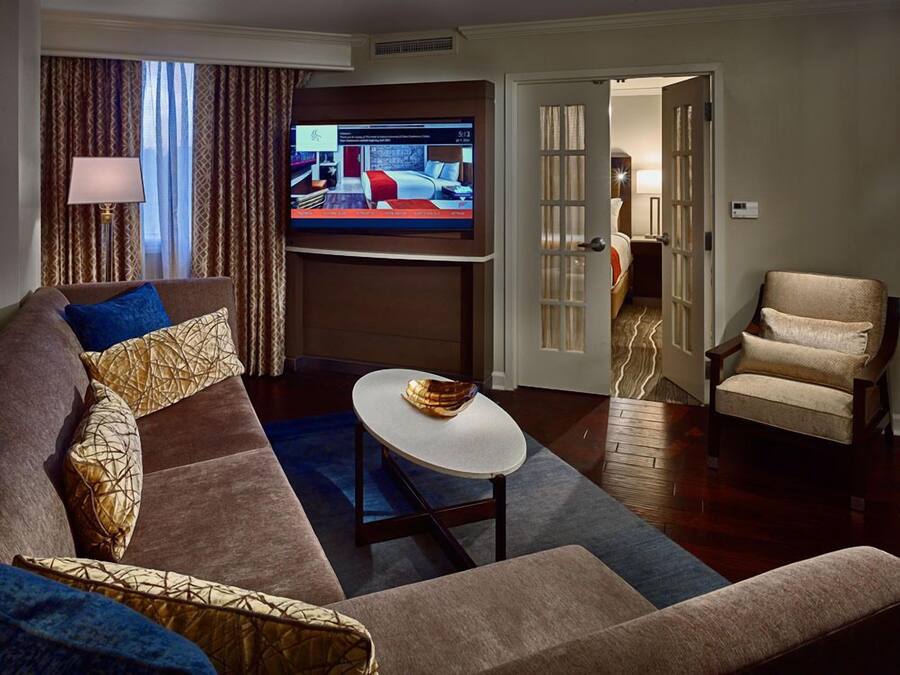 A modern living room with a large flat-screen TV, a sofa with patterned cushions, a round coffee table, and a chair.