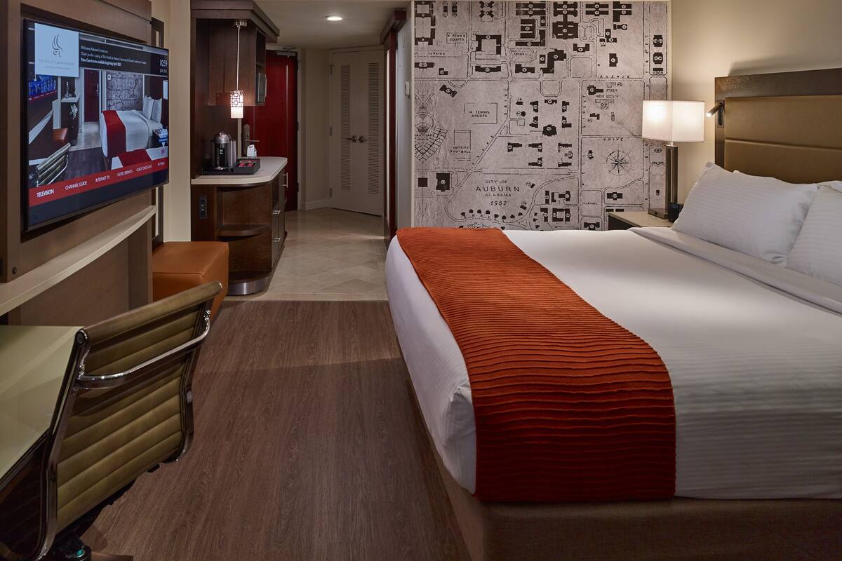 A hotel room with a large bed, a desk with a chair, a television, and a map on the wall.