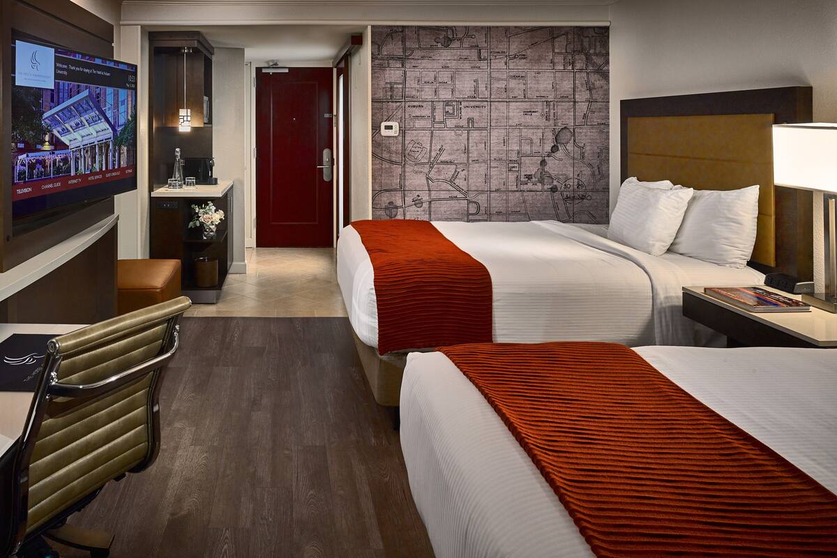 A hotel room with two beds, a TV, a desk, and a map on the wall.