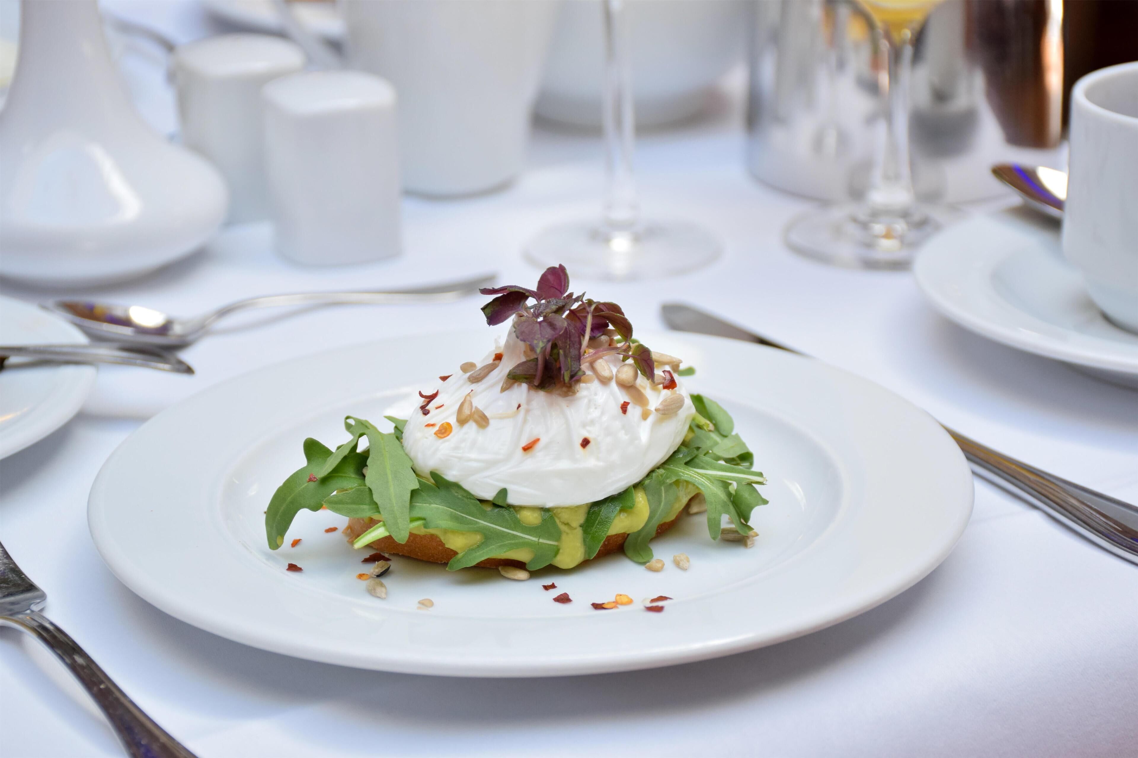 Une assiette blanche contenant un plat, une table dressée avec une nappe blanche et un verre à vin.