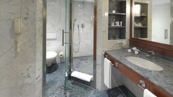 Ein modernes Badezimmer mit einer gläsernen Dusche, einem Marmorboden, einer Marmorwand, einem großen Spiegel und einem Waschbecken mit einer Granit-Arbeitsplatte.