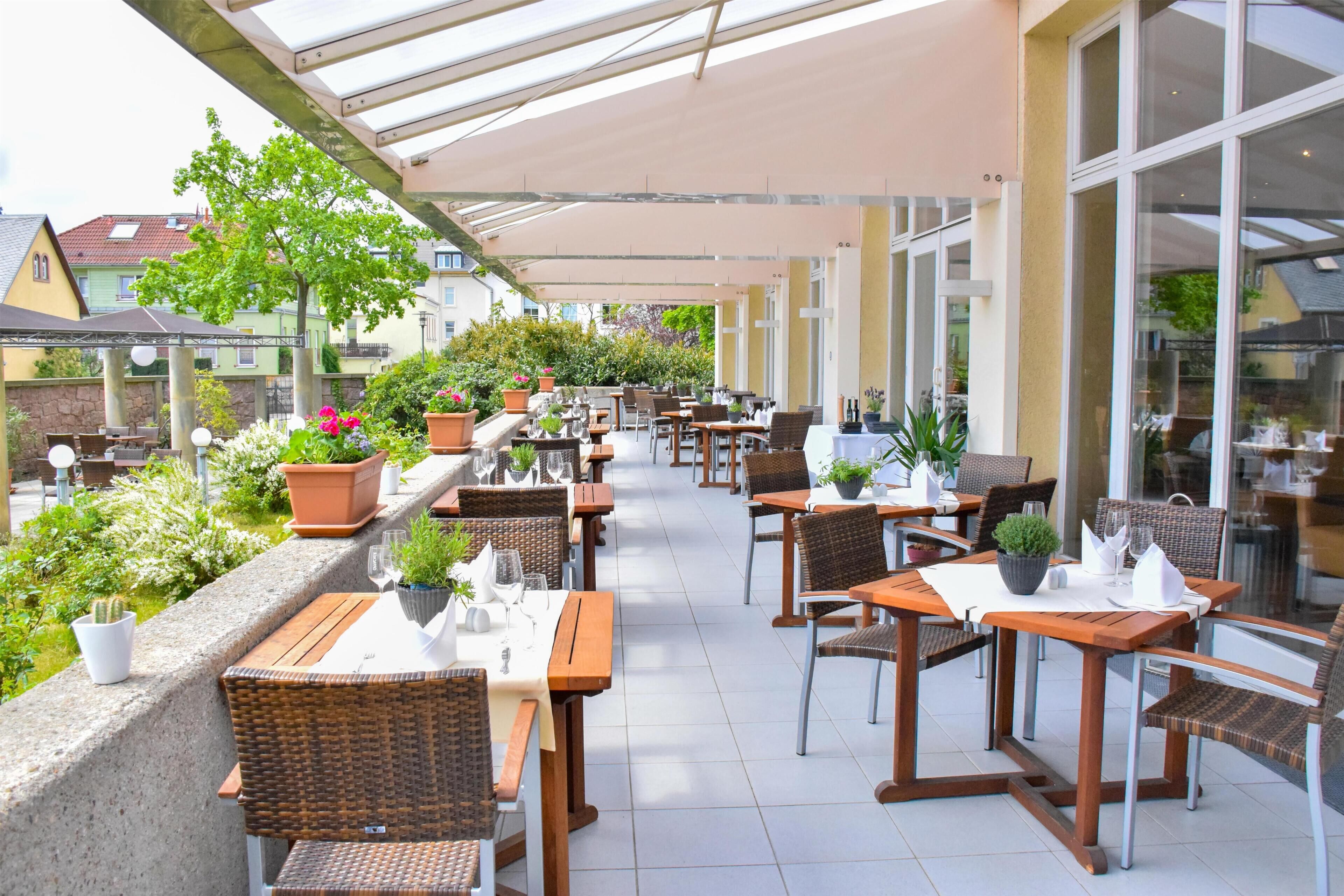 An outdoor café with tables and chairs, potted plants, and a view of the neighborhood.