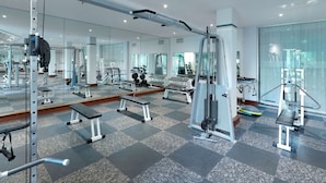Une salle de sport moderne équipée de divers appareils d’exercice, dotée de murs recouverts de miroirs et d’un sol à carreaux.