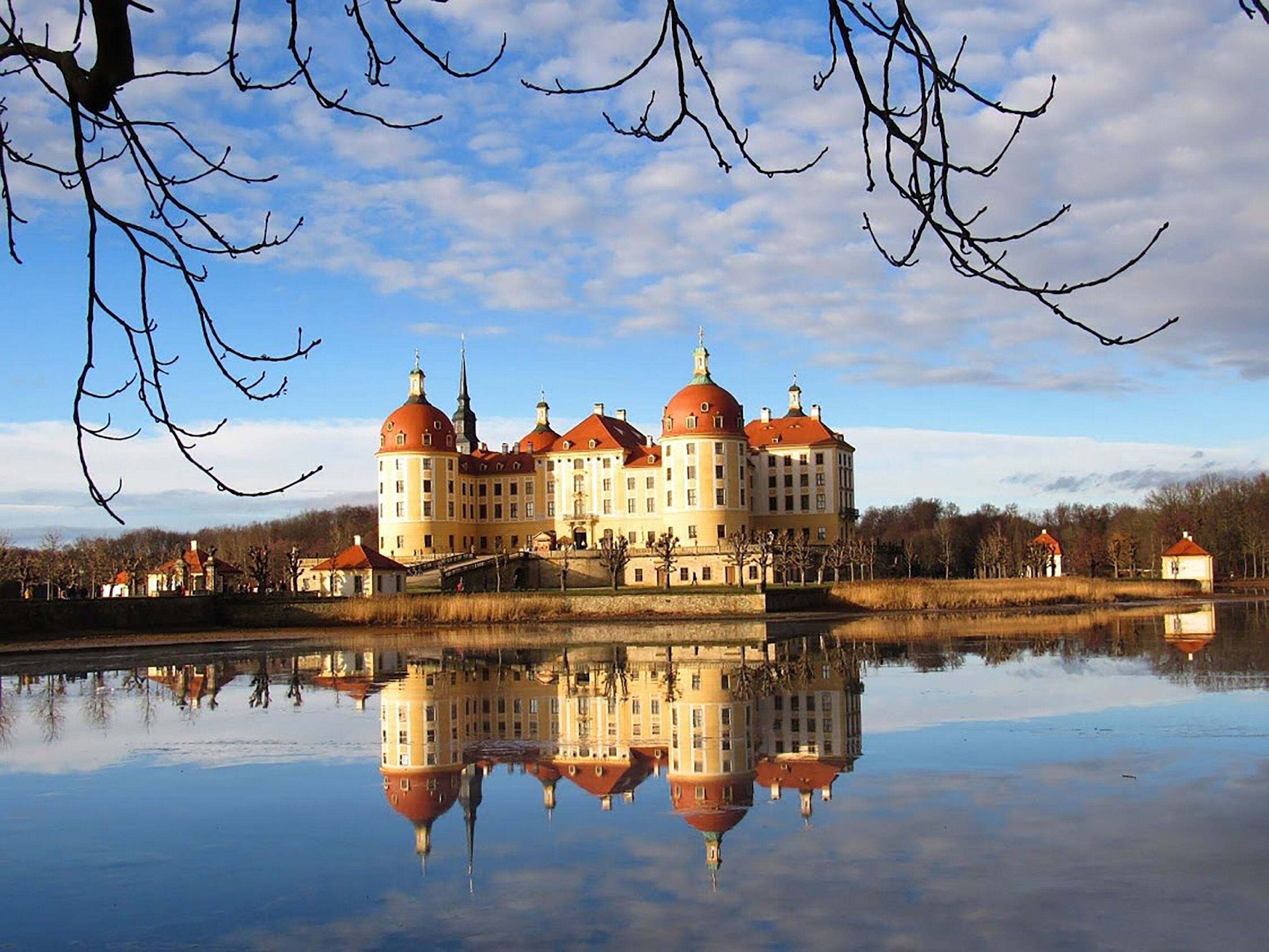 Ein großes, historisches Gebäude mit mehreren Kuppeln und Spiegelbild im Wasser.
