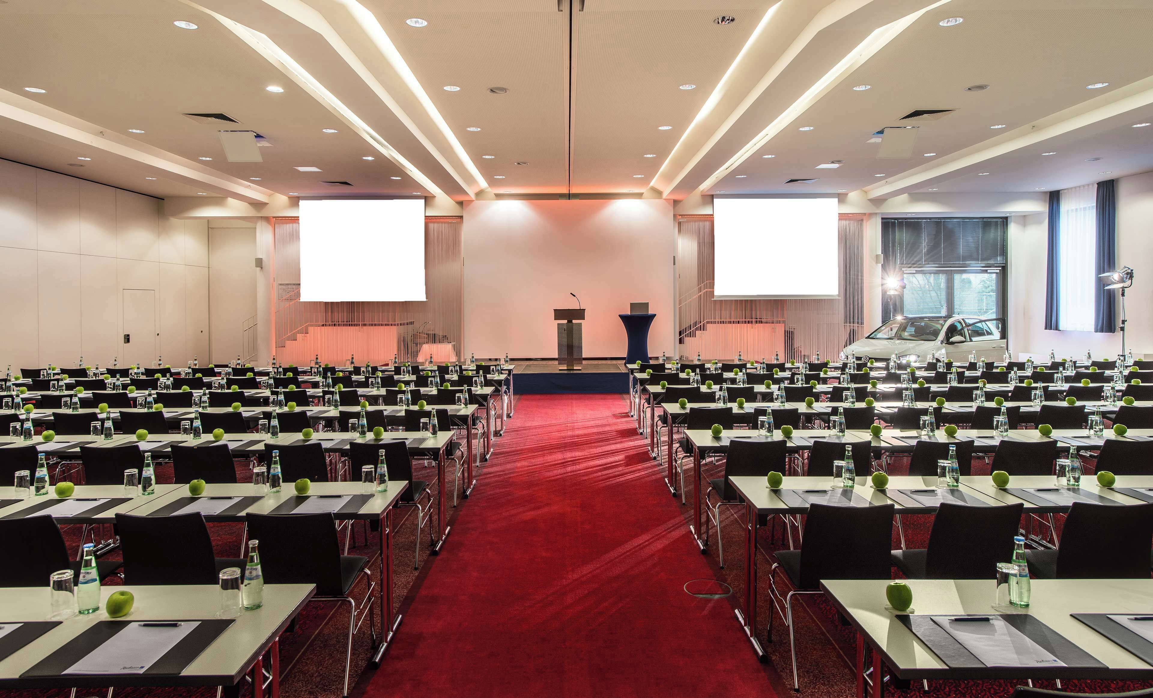 Un salón de conferencias con filas de mesas, sillas y un atril al frente.