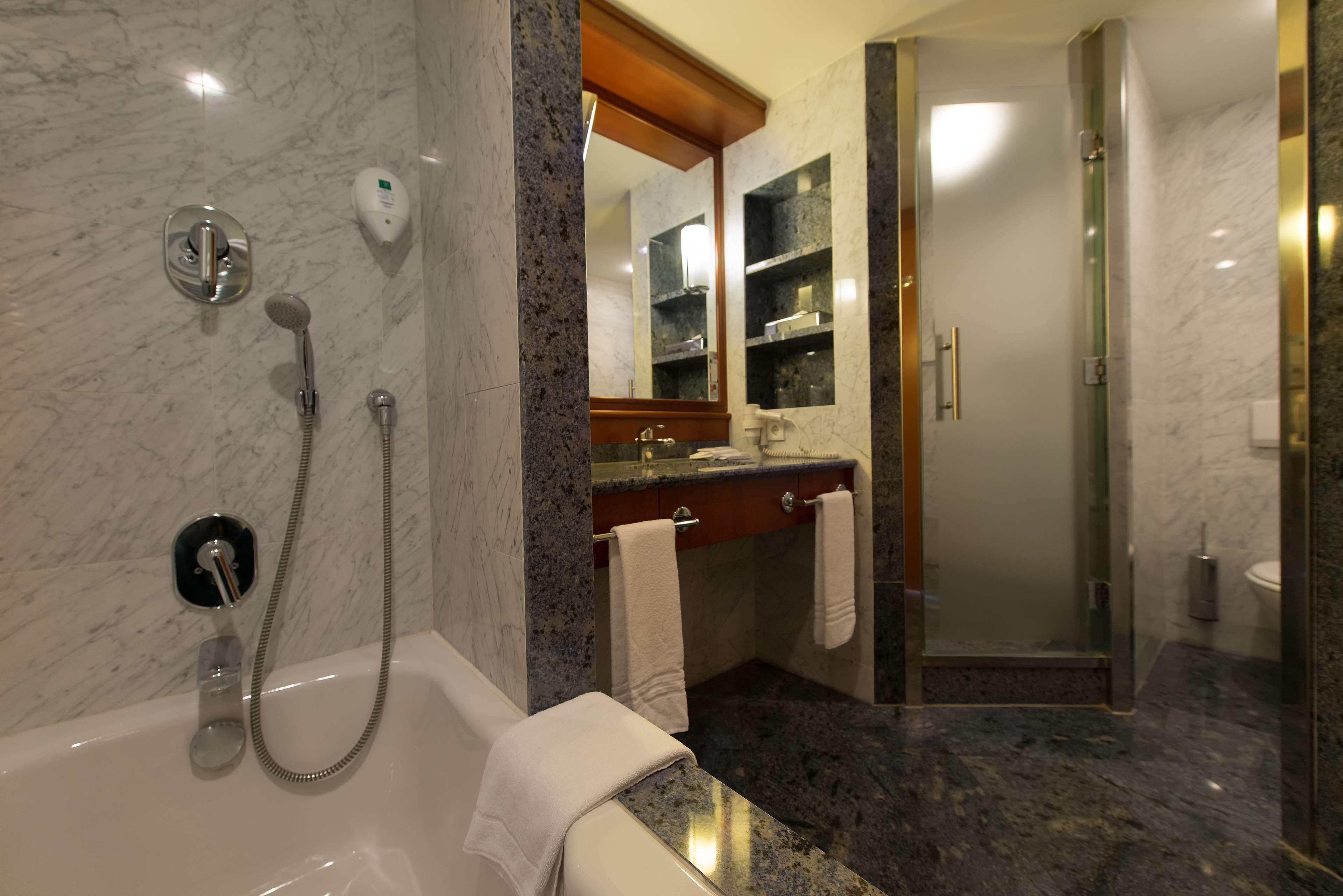 A modern bathroom with a marble vanity, a glass-enclosed shower, and a bathtub with a handheld showerhead.
