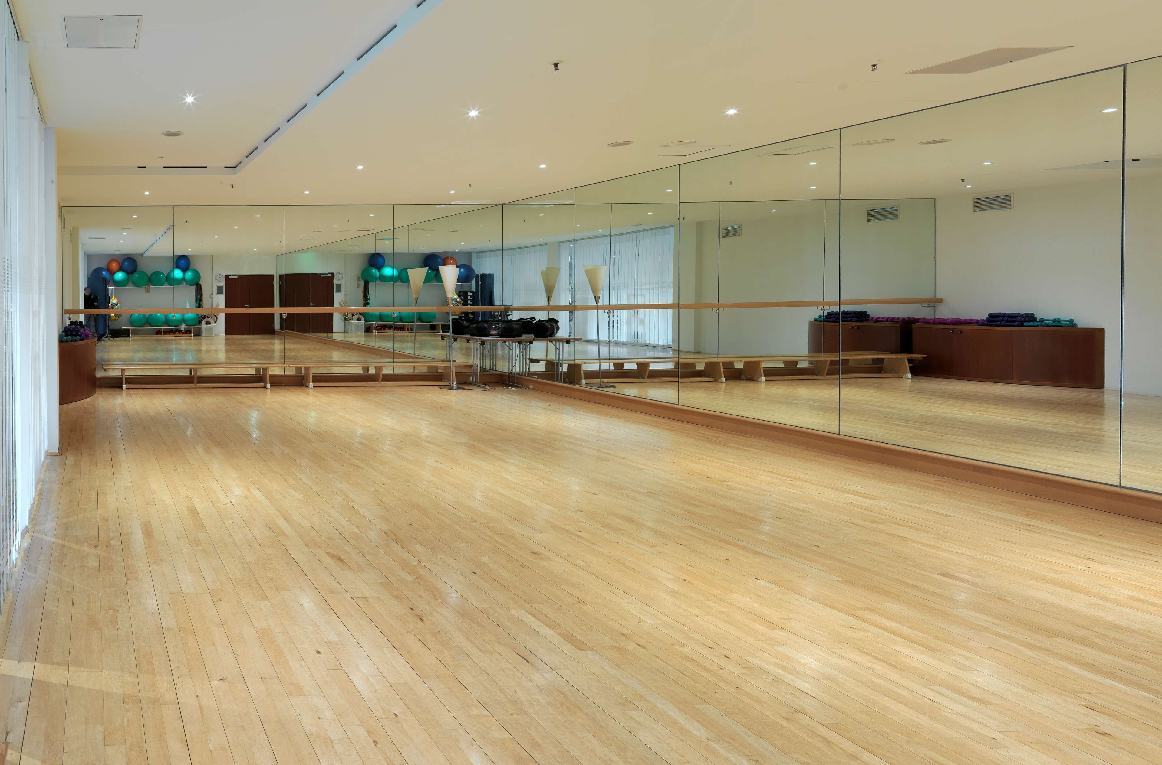 A spacious room with a wooden floor, large mirrors, and exercise equipment.