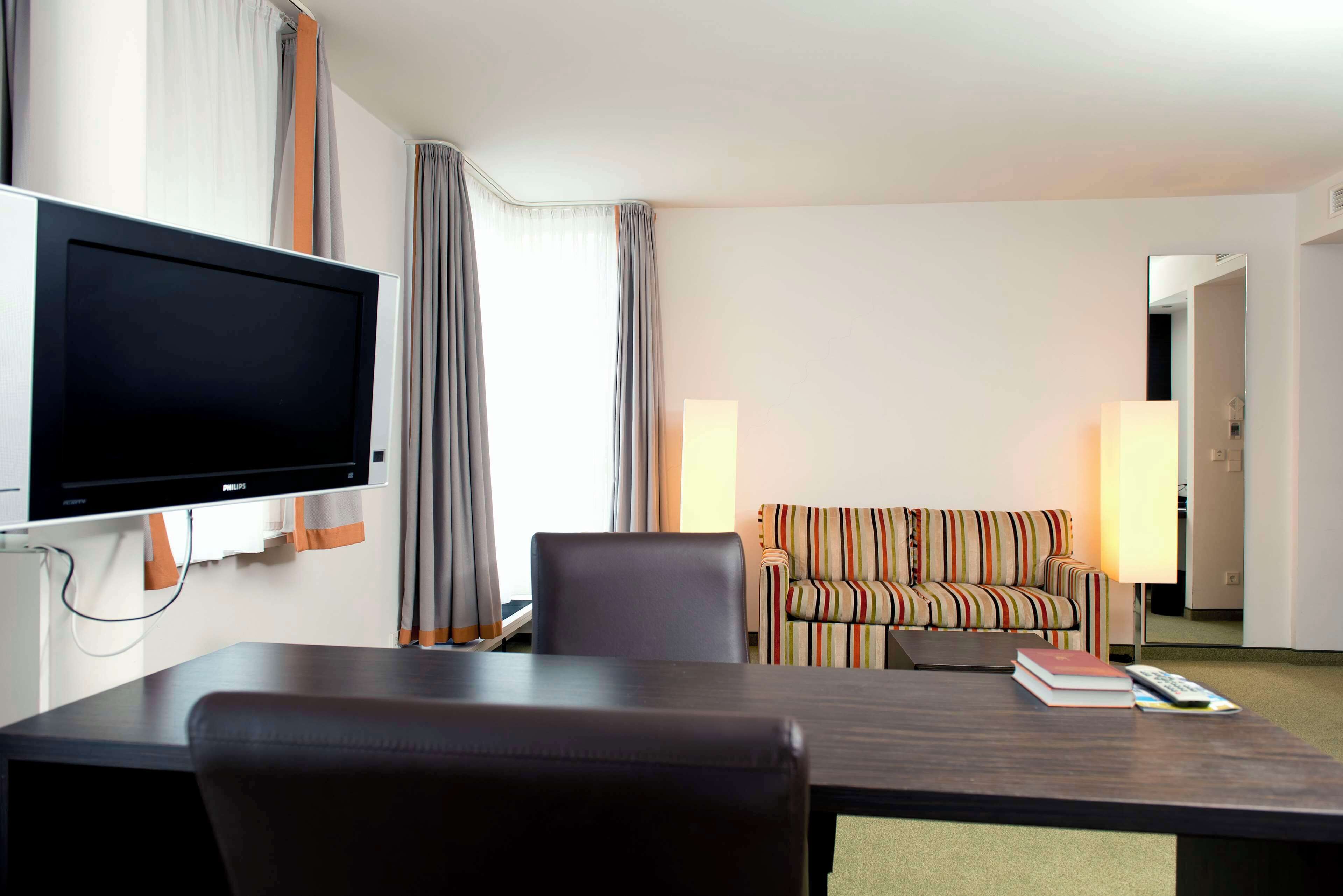 A hotel room with a TV, a striped sofa, a table, and two chairs.