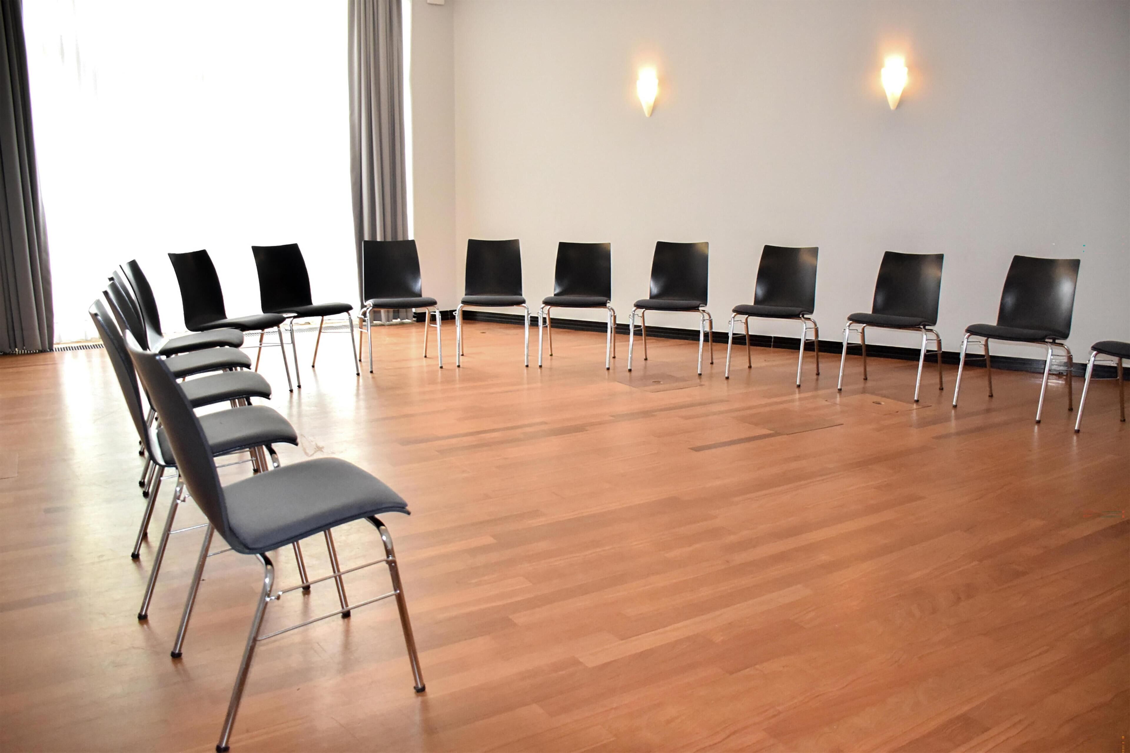 A conference room with rows of chairs, a wooden floor, and two wall-mounted lights.
