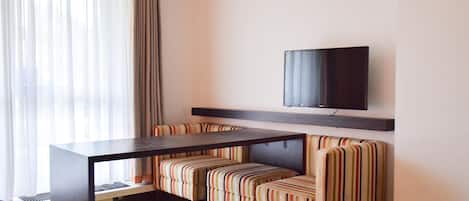 Una habitación de hotel con cama, escritorio, televisión en la pared y ventana con cortinas.