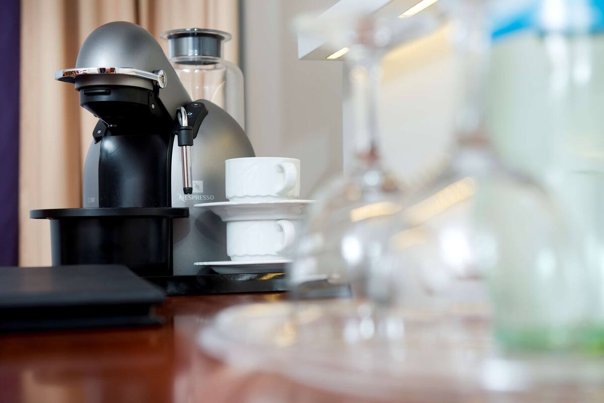 Una cafetera con taza y platillo, una jarra de vidrio y un dispensador de agua sobre una mesa de madera.