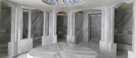 Un baño moderno con suelo de mármol, un lavamanos central y un techo con caligrafía azul decorativa.