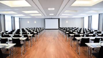 Ein Konferenzraum mit Reihen von Tischen und Stühlen, einer großen Leinwand an der Stirnseite und einem Holzboden.