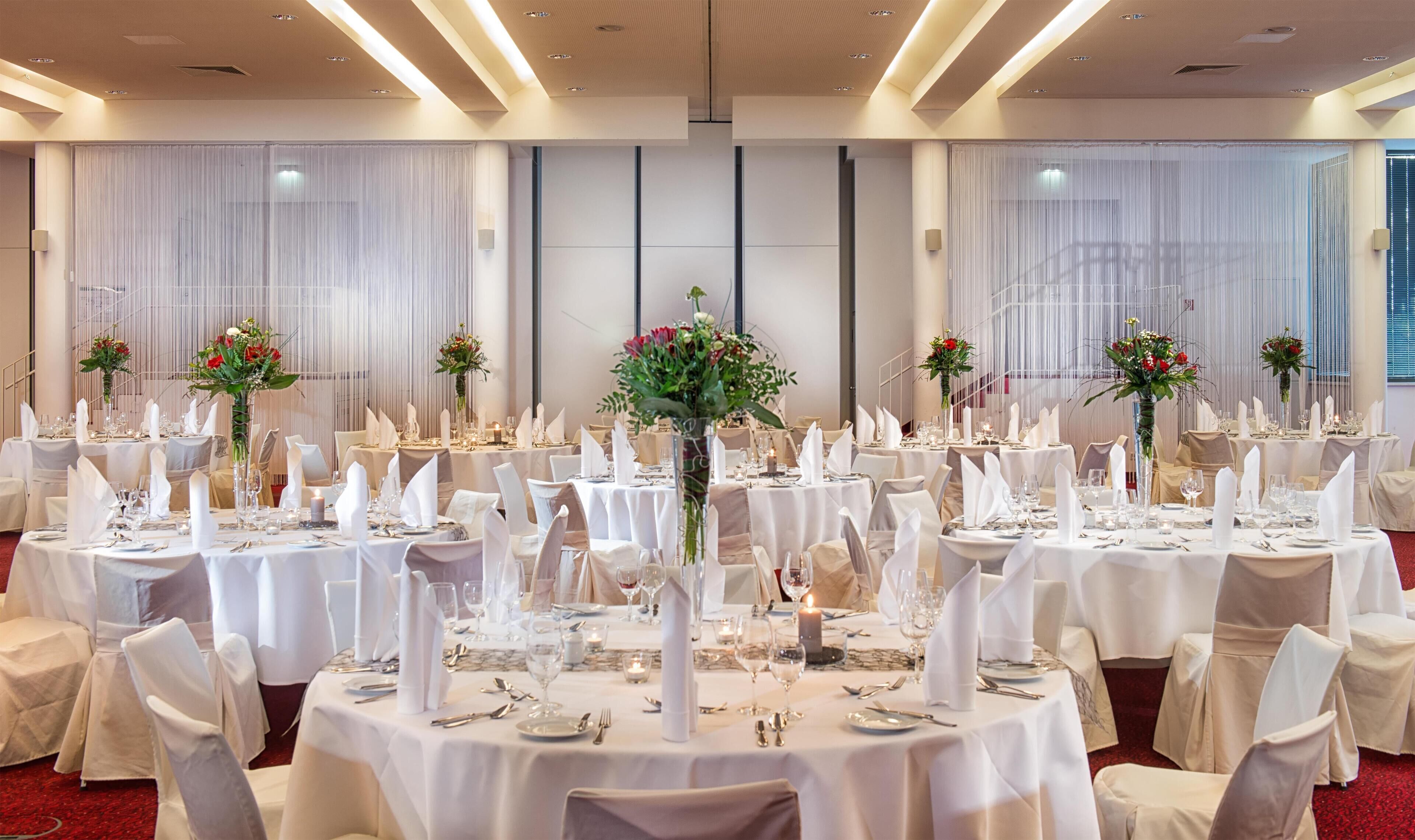 Un salón de banquetes con mesas redondas dispuestas para un evento formal, con manteles blancos, sillas y centros de mesa florales.