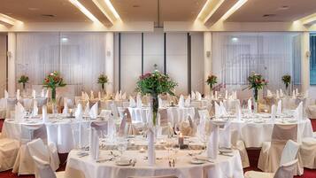 Un salón de banquetes con mesas redondas dispuestas para un evento formal, con manteles blancos, sillas y centros de mesa florales.