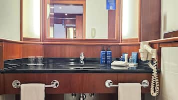 A bathroom with a wooden vanity, a mirror, a sink with a black countertop, two towels, a trash can, and a telephone.