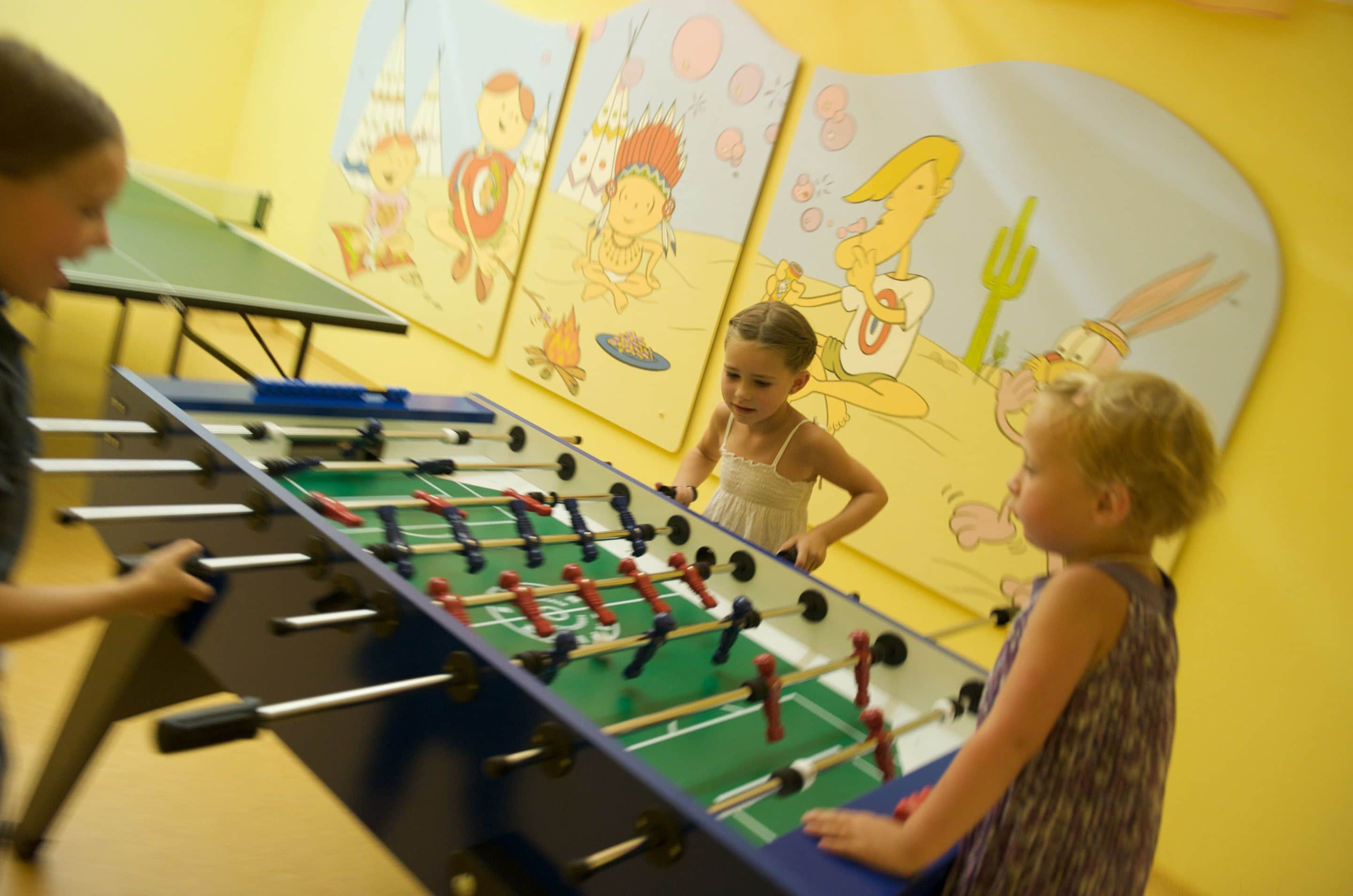 Une table de baby-foot dans une pièce aux murs jaunes, décorée de fresques murales représentant des personnages de dessins animés.