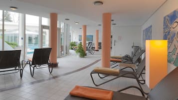 A spacious indoor area with large windows, a pool, and several lounge chairs.