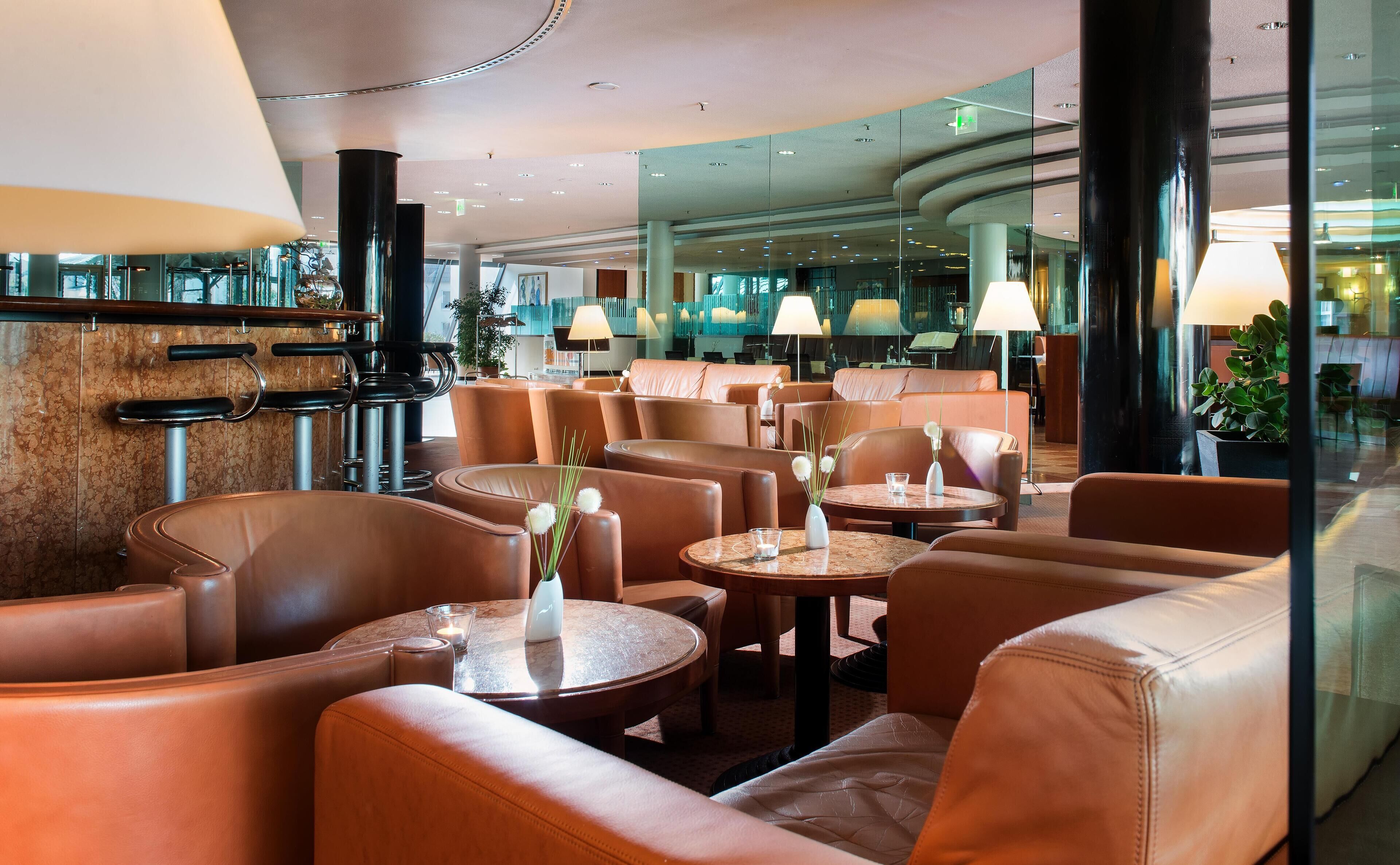 A modern hotel lobby with leather seating, round tables, and ambient lighting.