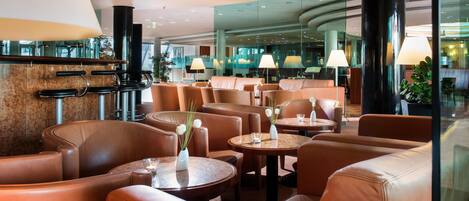 Eine moderne Hotelhalle mit Ledersitzmöbeln, runden Tischen und stimmungsvoller Beleuchtung.