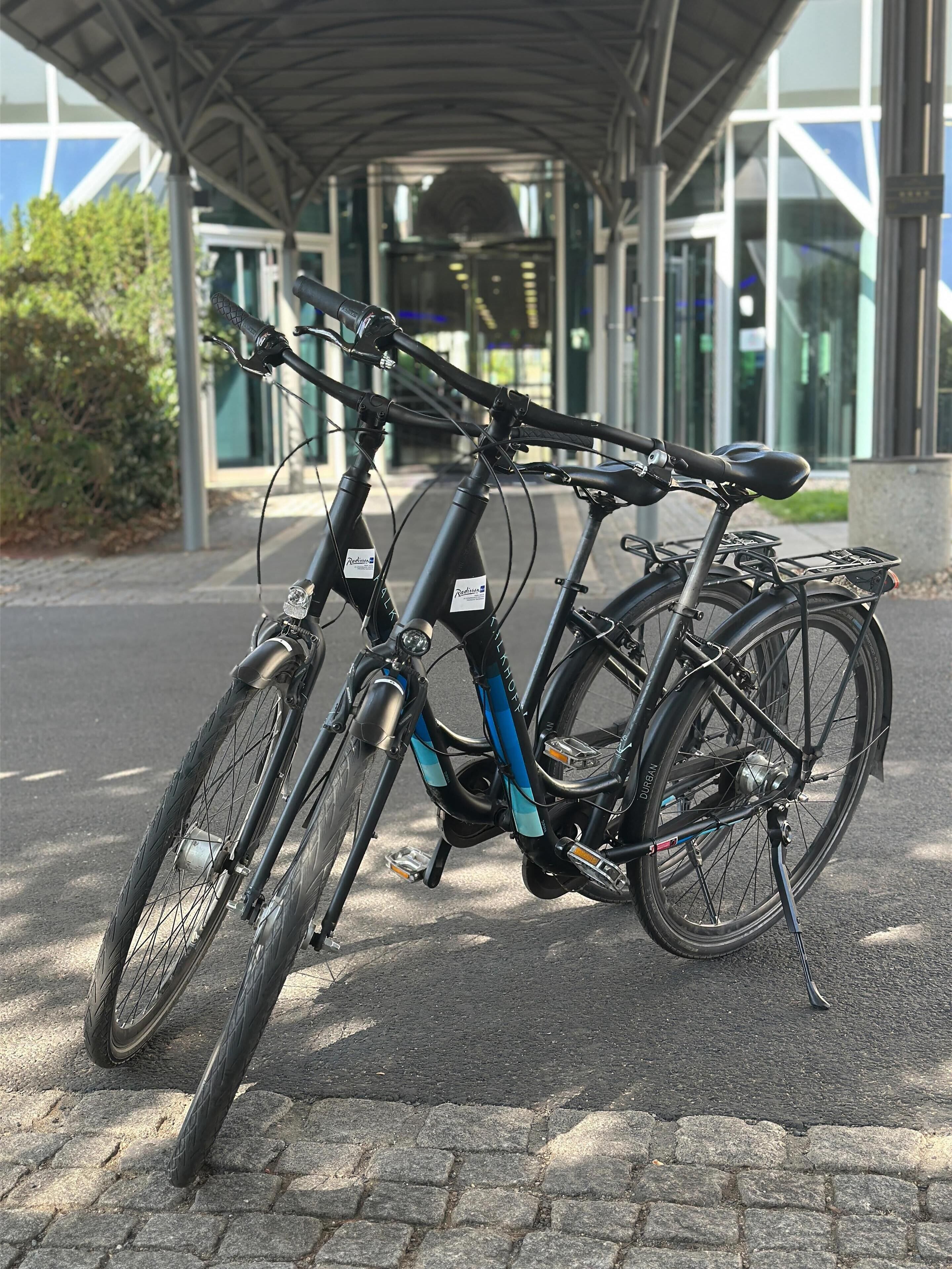 Ein Fahrrad steht unter einer Überdachung, im Hintergrund ein modernes Gebäude.