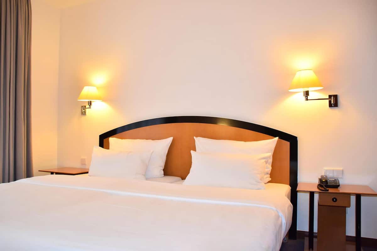 Una habitación de hotel con una cama grande, dos mesitas de noche y dos lámparas de pared.