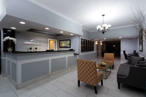 Een receptiegedeelte met een balie waarop de naam 'Howard Johnson' staat, een kroonluchter, zitplaatsen met gestreept bekleden meubilair en een televisiescherm.