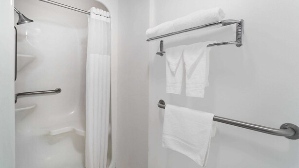 A bathroom with a bathtub, a shower, and a toilet. There are two towel racks with towels hanging on them. - Howard Johnson by Wyndham Waukegan Great Lakes (Waukegan)