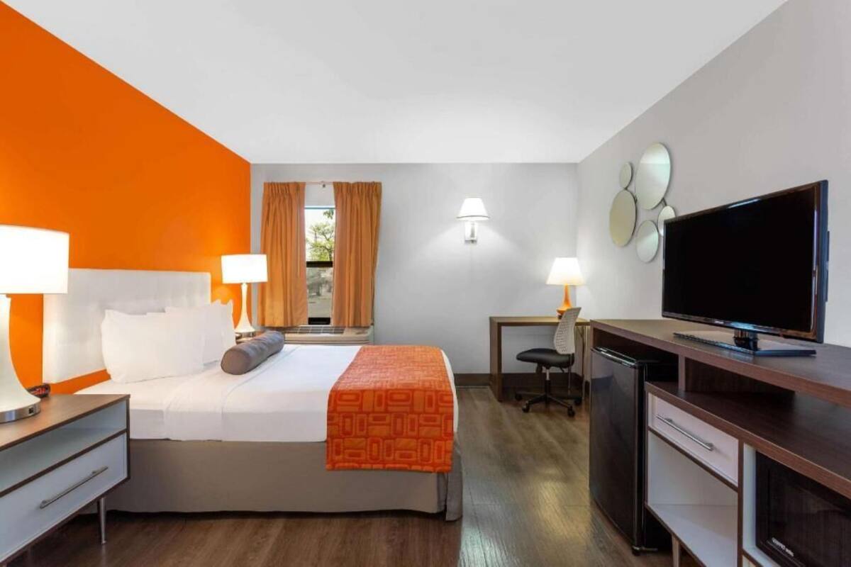Habitación de hotel con cama, escritorio, televisión y ventana con cortinas.