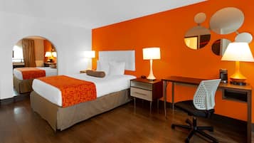 Habitación de hotel con cama, escritorio, silla y espejo en la pared.