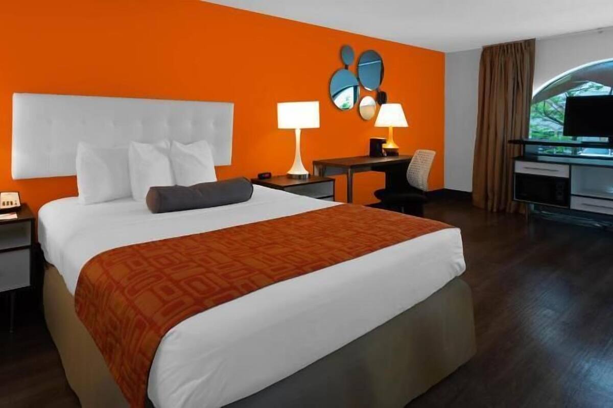 Una habitación de hotel con una cama grande, dos mesitas de noche, un escritorio con silla, un televisor y una ventana con cortinas.