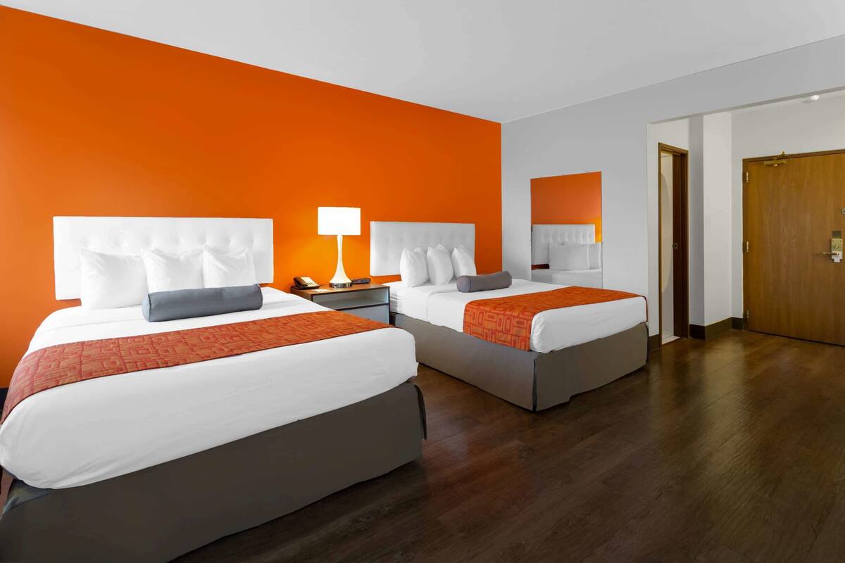 Una habitación de hotel con dos camas, una mesita de noche con lámpara y una puerta de madera.