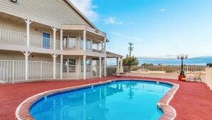 A swimming pool with a red deck, a two-story building with balconies, and a view of the ocean.