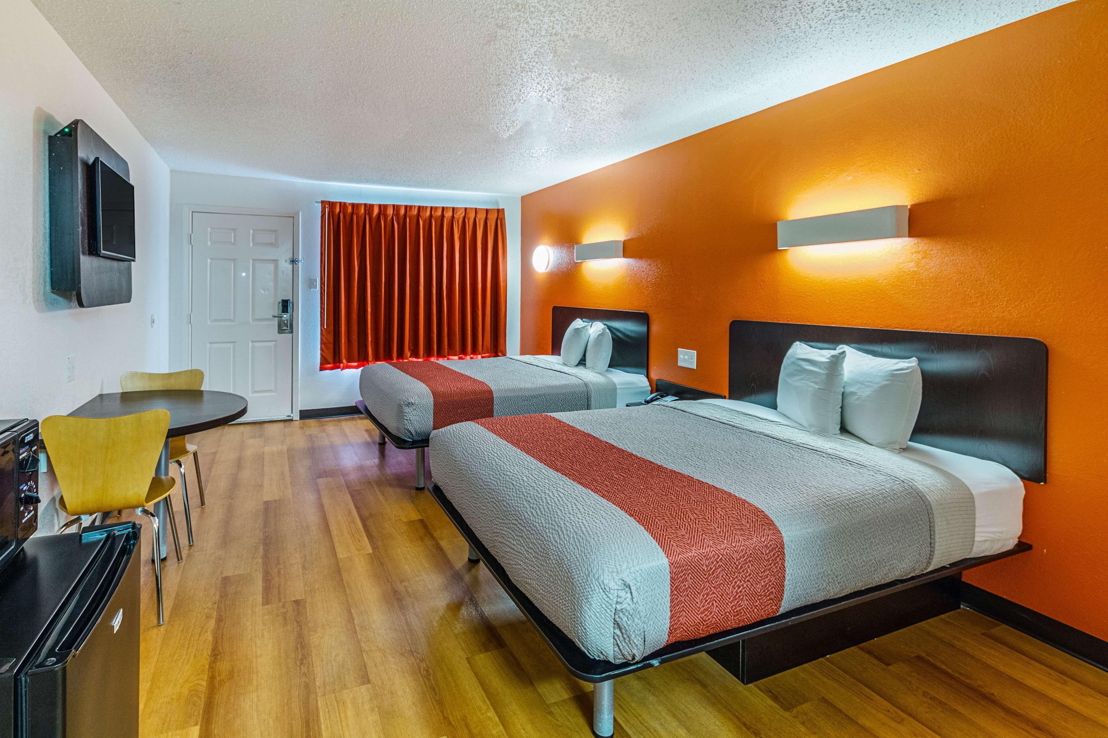 A hotel room with two beds, a TV, a desk, and a dining area.