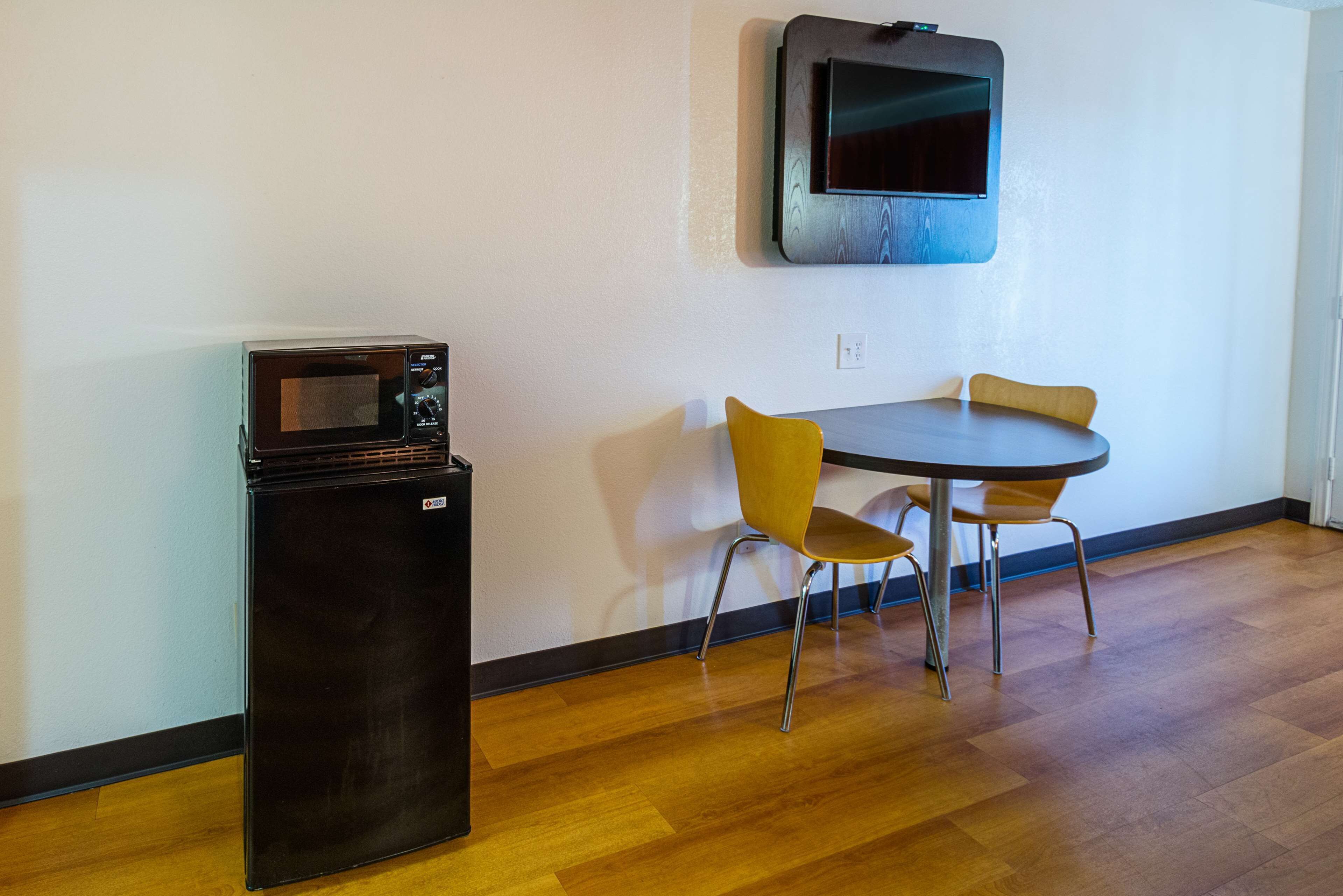 A compact kitchenette with a microwave, a small refrigerator, and a dining area with two chairs and a table.