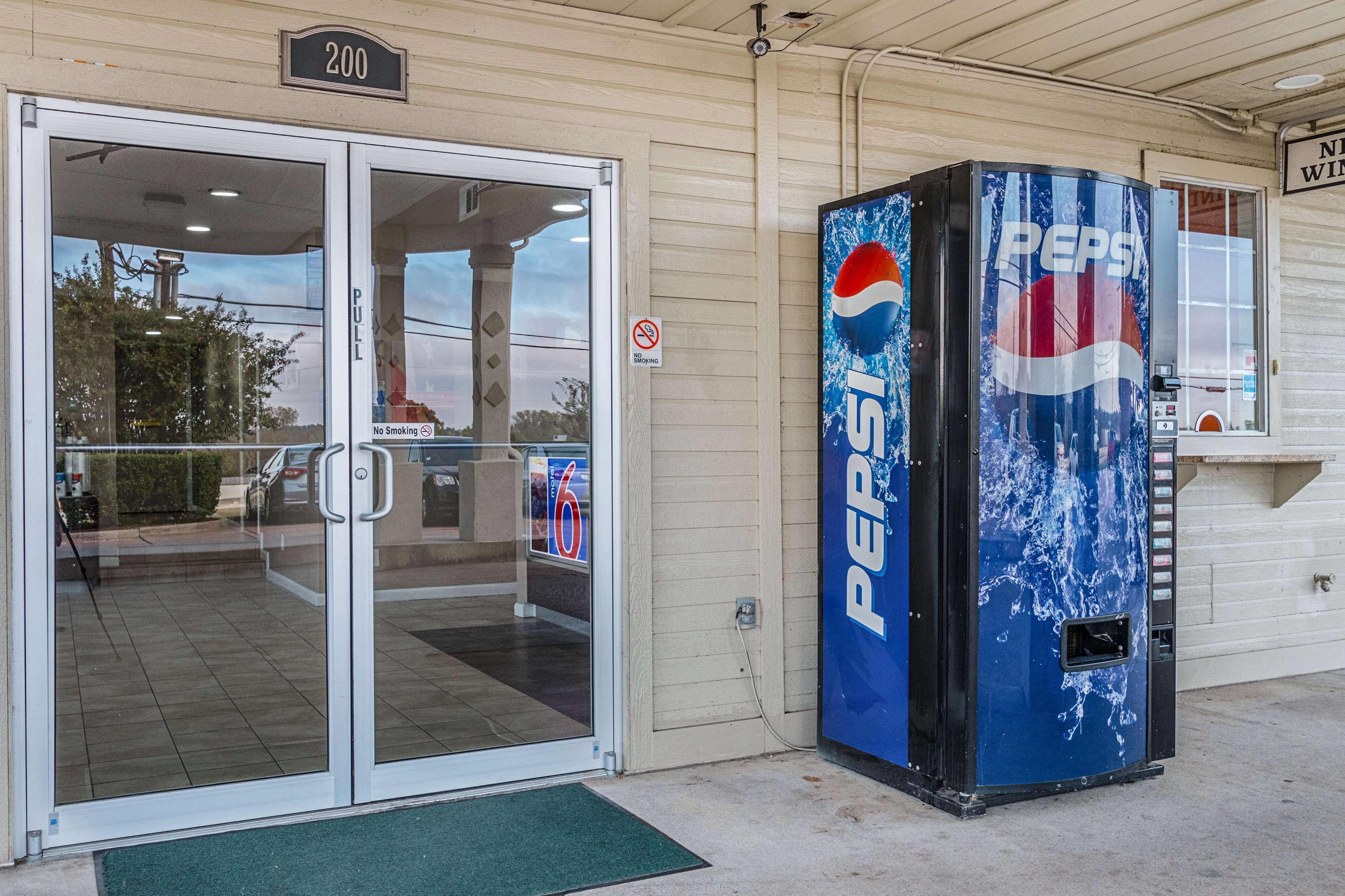 Een gebouwtoegang met een glazen deur, een Pepsi automaat en een rookvrij bord.