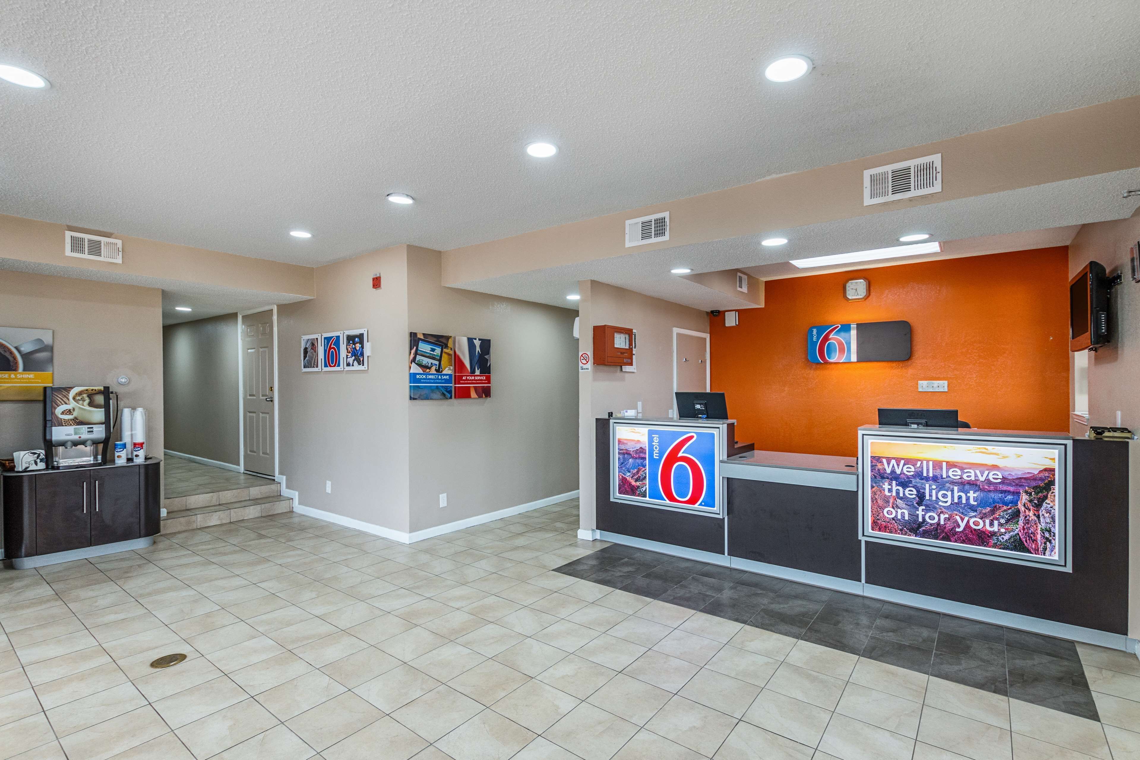 A hotel reception area with a reception desk, a digital display, and a sign that reads "We'll leave the light on for you."