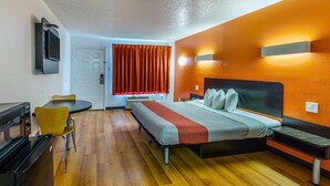 A hotel room with a bed, bedside tables, a desk with a chair, a TV mounted on the wall, and a window with curtains.