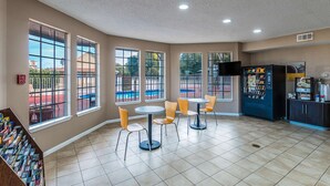 A spacious indoor area with large windows, multiple tables and chairs, a vending machine, and a television.