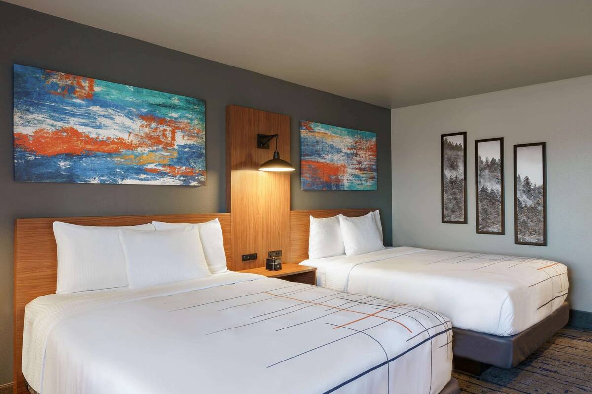 A hotel room with two beds, a wooden headboard, and artwork on the walls.