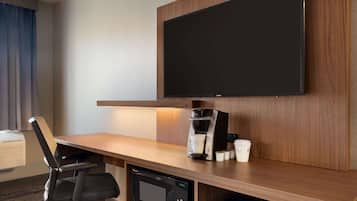 Habitación de hotel con un escritorio de madera, un televisor de pantalla plana montado en la pared, una cafetera y un microondas.