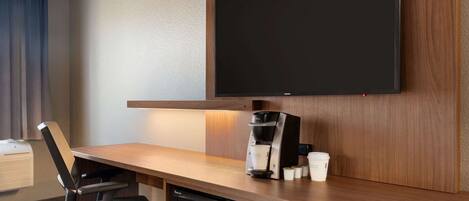 Habitación de hotel con un escritorio de madera, un televisor de pantalla plana montado en la pared, una cafetera y un microondas.