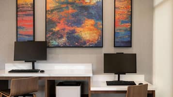 Un espacio de oficina moderno con dos escritorios, cada uno con monitor, teclado y ratón. Hay tres grandes cuadros abstractos en la pared sobre los escritorios.
