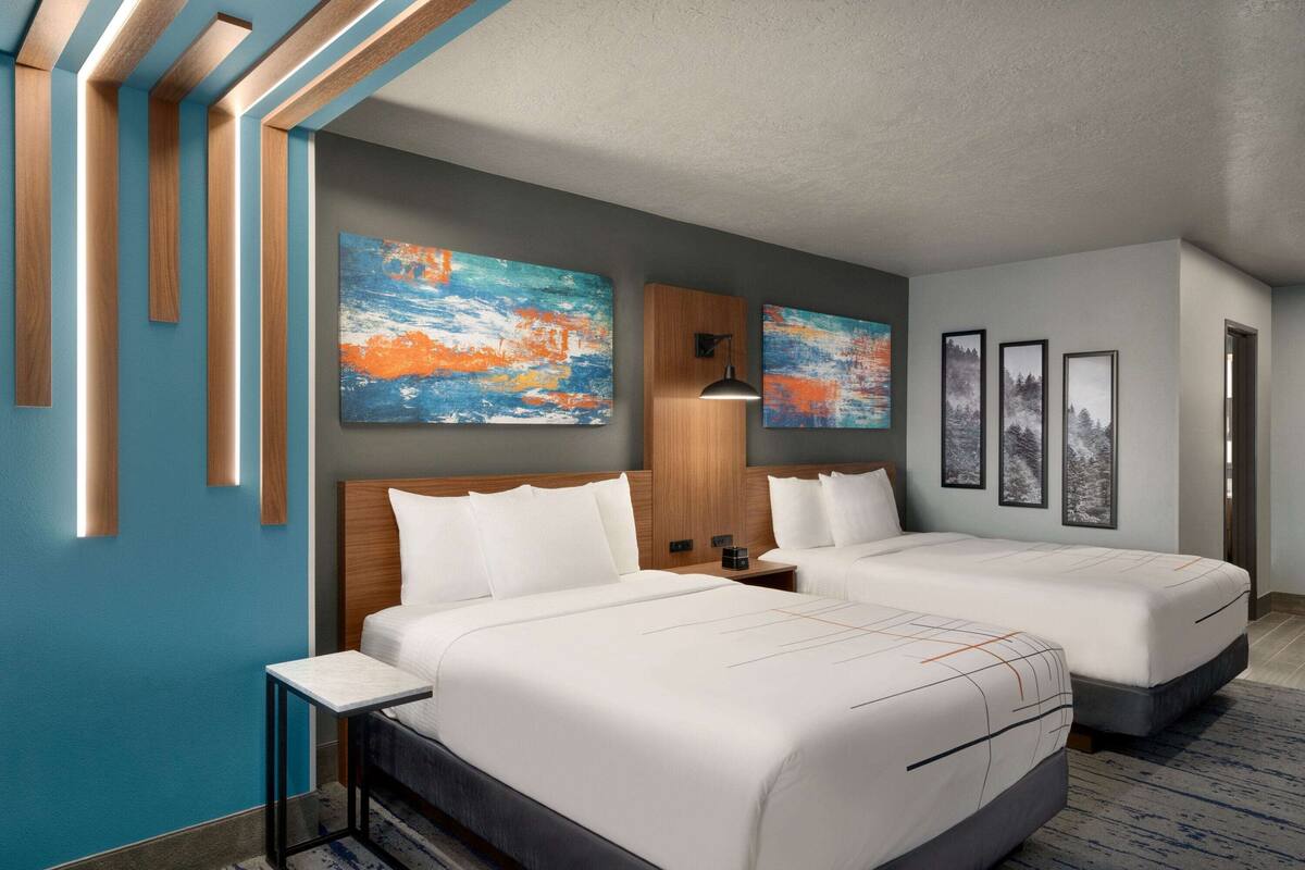A hotel room with two beds, a wooden headboard, a nightstand, a table, and artwork on the walls.