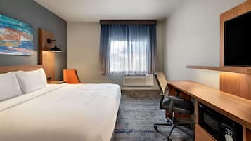 Et hotelværelse med en stor seng, et skrivebord, en aircondition, et fjernsyn og et vindue med gardiner.