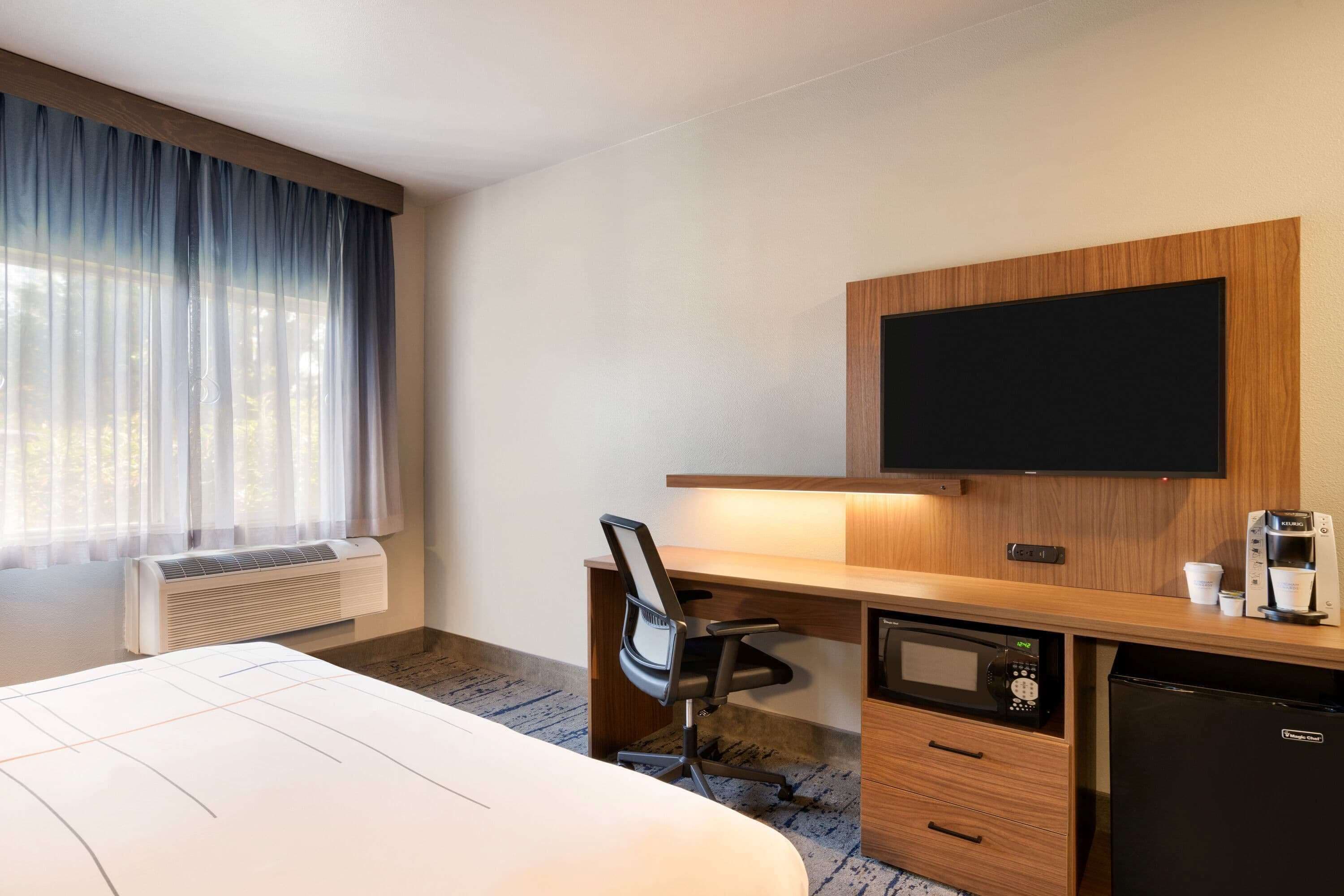 A hotel room with a bed, a desk with a chair, a television, a coffee maker, a microwave, and a refrigerator.