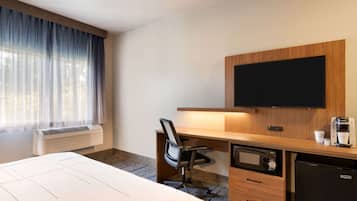 A hotel room with a bed, a desk with a chair, a television, a coffee maker, a microwave, and a refrigerator.